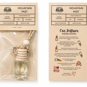 May include: A clear glass car air freshener bottle with a light wood cap and a beige and gold cord, packaged in a plastic sleeve with a tan header card labeled Mountain Mist, Hand Poured in PA, 8ml, and a separate instruction card.