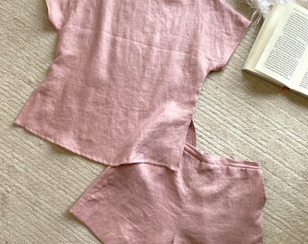 May include: A blush-pink sleepwear set comprising a short-sleeved top and shorts. The top features a round neck and side slits, while the shorts have an elasticated waistband. The set is made from a soft, flowing fabric, perfect for relaxing.