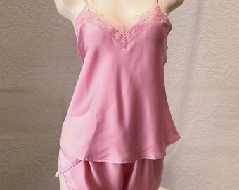 Könnte beinhalten: Hellrosa Satin-Pyjama-Set auf einer Schaufensterpuppe. Das Set besteht aus einem Camisole mit zarter Spitzenborte und passenden Shorts. Der Stoff hat einen subtilen Glanz, der auf ein luxuriöses Gefühl hindeutet.