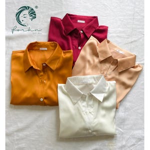 Könnte beinhalten: Vier Satinhemden in verschiedenen Farben: Rot, Orange, Beige und Weiß. Jedes Hemd hat einen Knopfkrag und lange Ärmel.