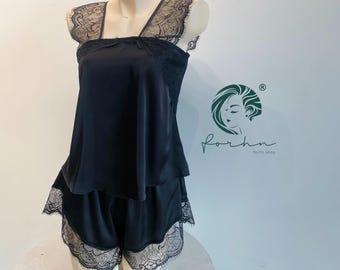 Puede incluir: Un conjunto de pijama negro de dos piezas compuesto por una camiseta sin mangas y pantalones cortos a juego. Ambas piezas tienen un acabado satinado suave y están adornadas con encaje floral negro en el escote, los tirantes y los bordes.