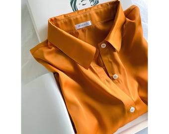 May include: A mustard yellow button-down shirt with a classic collar and white buttons. The shirt features a label at the neckline with the text "fardus | L". The garment is folded neatly inside a white box, which displays a dark green logo.