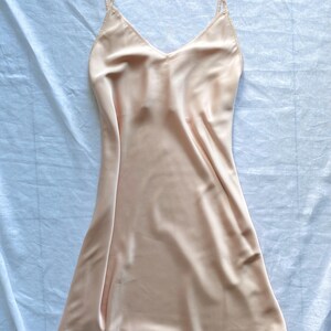 K&ouml;nnte beinhalten: Ein hellpfirsichfarbenes Satin-Schlafkleid mit d&uuml;nnen Tr&auml;gern.