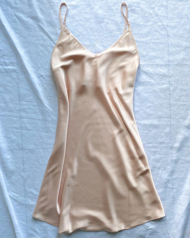 K&ouml;nnte beinhalten: Ein hellpfirsichfarbenes Satin-Schlafkleid mit d&uuml;nnen Tr&auml;gern.