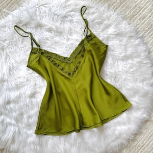 Pode incluir: Top camisola verde-oliva com finas alças espaguete e decote em V. O decote é adornado com uma babado decorativo. O tecido sedoso cai suavemente. A parte superior é de cor sólida.
