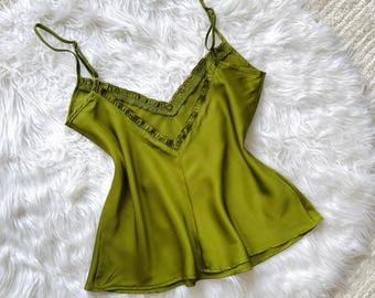 Könnte beinhalten: Olivgrünes Camisole-Top mit dünnen Spaghettiträgern und V-Ausschnitt. Der Ausschnitt ist mit einer dekorativen Rüsche verziert. Der seidige Stoff fällt weich. Das Top ist einfarbig.