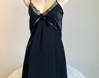 Könnte beinhalten: Schwarzes Satin-Slip-Kleid mit zarten Spaghettiträgern und V-Ausschnitt. Der Ausschnitt und das Oberteil sind mit filigraner Spitze verziert. Das Kleid wird auf einer Schaufensterpuppe vor neutralem Hintergrund präsentiert.