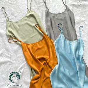 Può includere: Quattro abiti slip in seta di diversi colori: verde chiaro, grigio, arancione e azzurro. Gli abiti hanno spalline sottili e una scollatura rotonda.