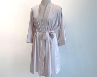 Könnte beinhalten: Helllila Satin-Bademantel mit passendem Gürtel, auf einer Schaufensterpuppe präsentiert. Der Bademantel hat lange Ärmel mit kontrastierendem Besatz und einen Schalkragen. Der Stoff hat einen dezenten Glanz.