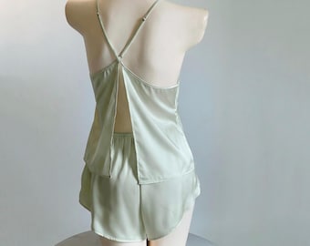 Könnte beinhalten: Ein hellgrünes Satin-Pyjama-Set. Das Oberteil hat einen V-Ausschnitt mit dünnen Trägern, die sich am Rücken kreuzen. Die Shorts sind in einem passenden hellgrünen Farbton gehalten. Das Set wird auf einer Schaufensterpuppe präsentiert.