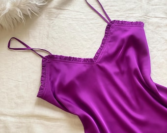Könnte beinhalten: Ein leuchtend magentafarbenes Slip-Kleid mit V-Ausschnitt und zartem Rüschenbesatz an den Kanten. Das Kleidungsstück ist aus einem glatten, satinartigen Stoff gefertigt und verfügt über dünne, verstellbare Spaghettiträger für eine schlichte Silhouette.