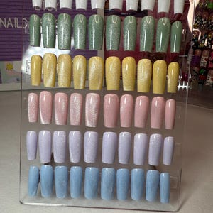 May include: A display of 10 rows of press-on nails with a variety of colors and glitter finishes. The colors include white, green, yellow, pink, lavender, and blue.