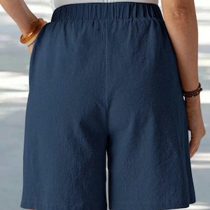 May include: Navy blue shorts with an elastic waistband. The shorts are made of a textured fabric and have a relaxed fit. The shorts are knee-length and have pockets. The model is wearing a white top and a bracelet.