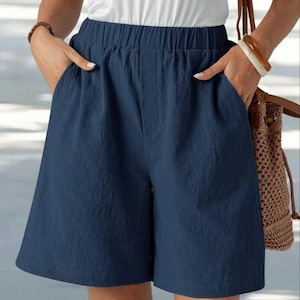 May include: Navy blue shorts with an elastic waistband and pockets. The shorts are made of a textured fabric and have a relaxed fit. The shorts are shown with a white top.