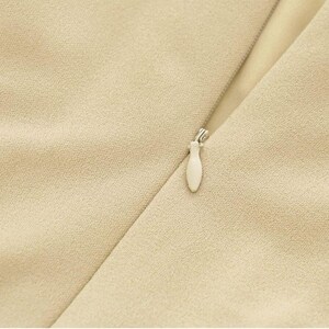Puede incluir: Primer plano de una prenda de vestir de tela beige con una cremallera y un tirador de cremallera blanco.
