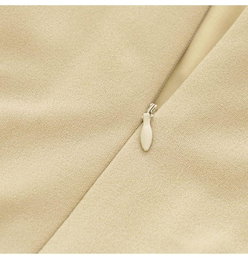 Puede incluir: Primer plano de una prenda de vestir de tela beige con una cremallera y un tirador de cremallera blanco.