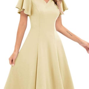 Puede incluir: Un vestido amarillo claro, de largo hasta la rodilla, con escote en V y mangas cortas con volantes.