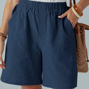 May include: Navy blue shorts with an elastic waistband and side pockets. The shorts are made of a textured fabric and appear to be lightweight. The shorts are part of a casual outfit.