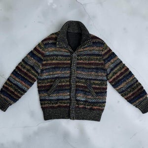 May include: A long-sleeve knit cardigan featuring a multi-colored horizontal striped pattern in shades of blue, burgundy, green, and gold. The garment has a thick ribbed collar, ribbed cuffs, a ribbed hem, and a front button closure with two pockets.