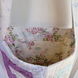 May include: A patchwork tote bag with a floral print lining. The bag is made from different fabrics, including a purple piece with frayed edges. The bag has a single strap and a small pocket inside.