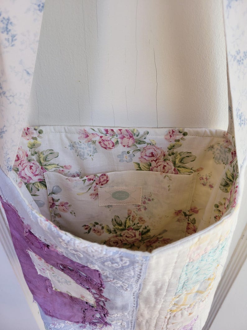 May include: A patchwork tote bag with a floral print lining. The bag is made from different fabrics, including a purple piece with frayed edges. The bag has a single strap and a small pocket inside.