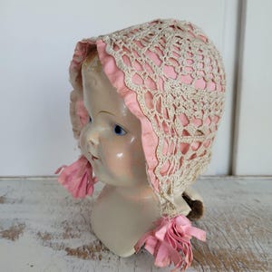 May include: A vintage porcelain doll head wearing a pink and white crocheted bonnet with pink ribbon ties.