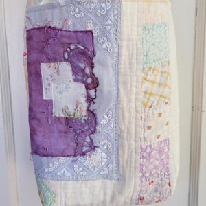 May include: A white patchwork tote bag with a purple and white floral design. The bag has a long strap and is made of various fabrics.