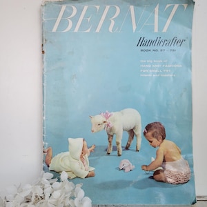 May include: Vintage "BERNAT Handicrafter" book cover featuring a light blue background with illustrations of babies and a lamb. The cover text reads "the big book of HAND KNIT FASHIONS FOR SMALL FRY infants and toddlers."