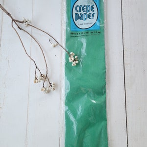 May include: A package of green crepe paper, flame resistant, by Dennison. The package says "Crepe Paper" in a blue circle with white lettering. The package also says "Flame Resistant" in smaller blue lettering.