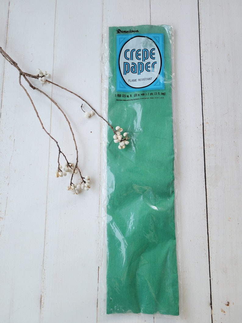 May include: A package of green crepe paper, flame resistant, by Dennison. The package says "Crepe Paper" in a blue circle with white lettering. The package also says "Flame Resistant" in smaller blue lettering.