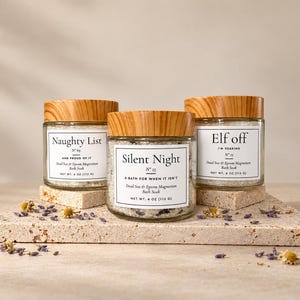 May include: Three clear glass jars with wood-grain lids containing bath soak. Labels read Naughty List, Silent Night, and Elf off. Each jar contains 4 oz (113 g) of Dead Sea and Epsom magnesium bath soak with visible dried flower petals.