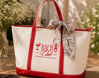 May include: A cream-colored canvas tote bag with red trim and handles. The front features red text reading BACH Club and Stephanie's Nashville Bash, with icons of a cocktail glass and a bottle. A patterned ribbon is tied to one handle.