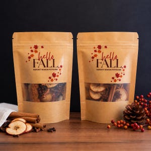 May include: Two stand-up kraft paper pouches containing harvest season potpourri. Each bag features a clear window, red and orange maple leaf graphics, and the text "hello FALL HARVEST SEASON POTPOURRI" printed in black and red ink.