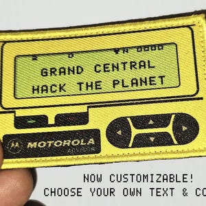 May include: A rectangular yellow embroidered patch designed to resemble a vintage Motorola pager. The screen displays the text GRAND CENTRAL HACK THE PLANET in black pixelated font. Below the screen are black control buttons and the Motorola logo.