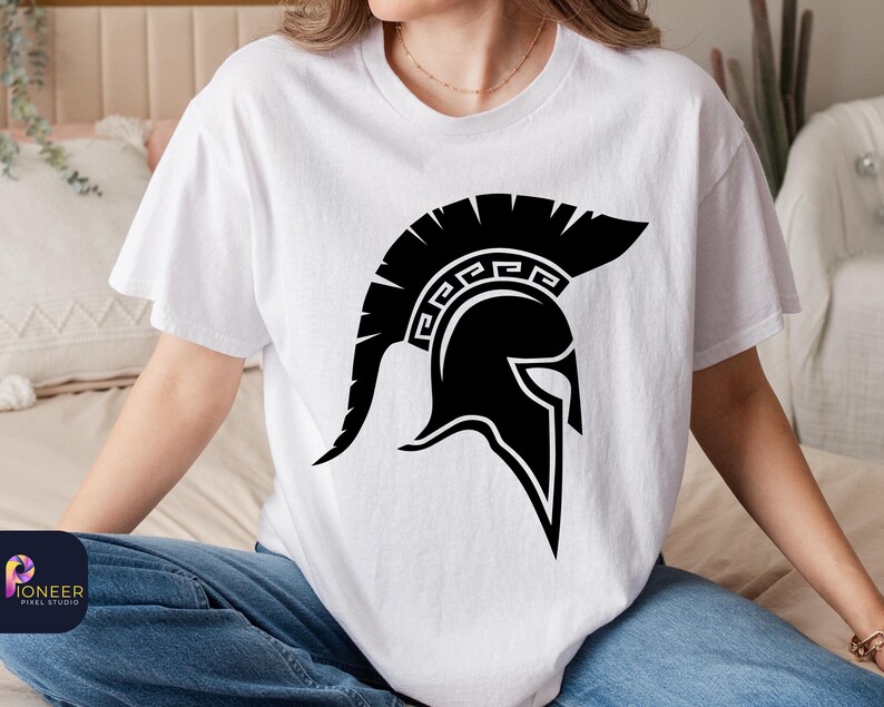 May include: A white t-shirt with a black graphic of a Spartan helmet. The helmet has a design of a Greek key pattern.