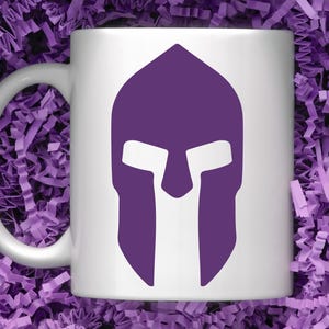 May include: White ceramic mug with a purple Spartan helmet graphic. The helmet is a silhouette with a white face mask.