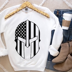 May include: White sweatshirt with a black and white graphic of an American flag inside a Spartan helmet.