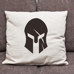 May include: A white pillow with a black silhouette of a spartan helmet in the center.