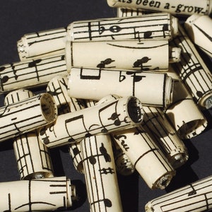 May include: A close-up of a pile of rolled up paper tubes with musical notes printed on them. The tubes are arranged in a random pattern and are all different lengths.