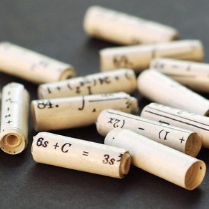 May include: A close-up of several small white paper tubes with black ink handwritten mathematical equations. The equations include numbers, variables, and symbols. One tube reads "6s + C = 3s3".