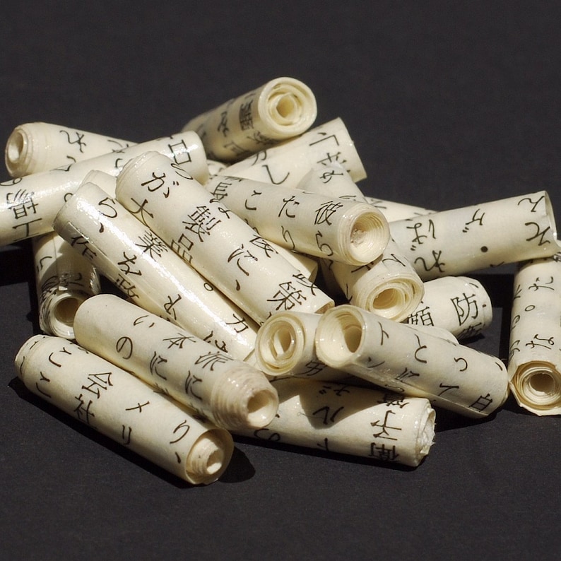 May include: A pile of rolled up paper scrolls with Japanese text printed on them. The scrolls are white and have a slightly textured surface.