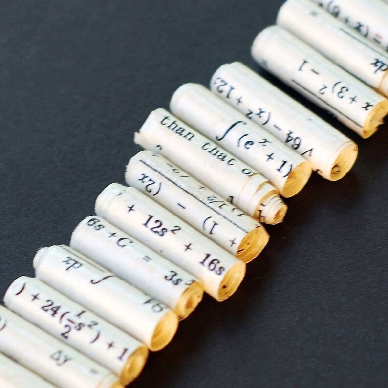 May include: A close-up of a row of rolled-up pieces of paper with mathematical equations written on them. The equations are in black ink and are visible on the white paper. The paper is rolled up tightly and the ends are visible.