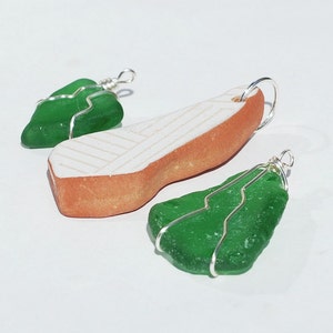 May include: Three handmade pendants, two are green sea glass wrapped in silver wire and one is a terracotta pendant with a white geometric design.
