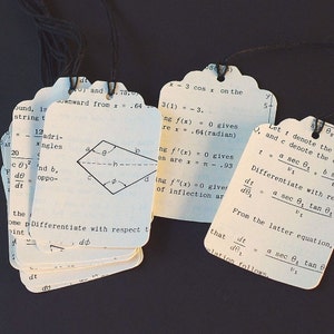 May include: A set of white index cards with handwritten mathematical equations and diagrams. The cards are stacked on top of each other and have a black string tied around them. The text on the cards includes the equations: x = 3 cos x, 3(1) = 3, f(x) = 0, f'(x) = 0, f''(x) = 0, t = a sec θ1, dt/dθ1 = a sec θ1 tan θ1, and dt/dθ1 = a sec θ1 tan θ1. The cards also include a diagram of a rhombus with the letters a, b, c, d, and h labeled on the sides and angles.