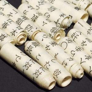 May include: Close-up of several rolled-up scrolls of paper with black Japanese characters printed on them. The scrolls are made of a light brown paper and are tied with a thin string.