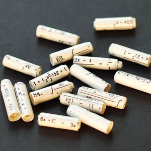 May include: A collection of white paper tubes with mathematical equations and numbers printed on them. The tubes are scattered on a black surface. The equations include integrals, derivatives, and algebraic expressions.