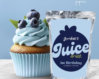 May include: A cupcake with pale blue icing, blueberries, and a blue paper case next to a juice drink pouch. The pouch has a blueberry graphic and text that reads "Jordan's Juice drink 1st Birthday Saturday, Sep 6th."