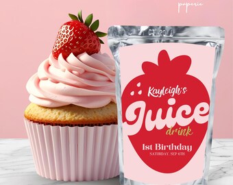 May include: A cupcake with pink icing and a fresh strawberry, beside a juice drink pouch. The pouch features a strawberry graphic and the text "Kayleigh's Juice drink 1st Birthday". The background is a solid pink.