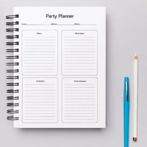 May include: A white party planner with a black spiral binding. The planner has sections for event details, menu, beverages, activities, and entertainment. The planner is on a grey surface with a blue pen and a white pencil.