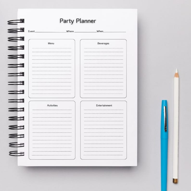 May include: A white party planner with a black spiral binding. The planner has sections for event details, menu, beverages, activities, and entertainment. The planner is on a grey surface with a blue pen and a white pencil.